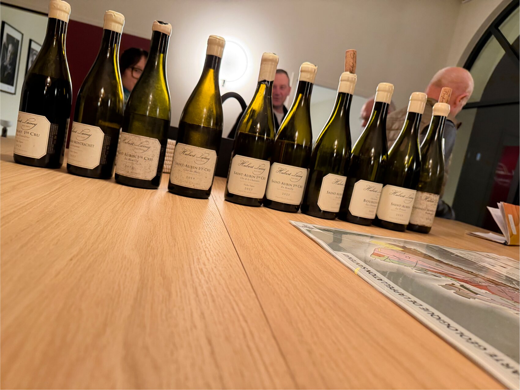 Dégustation au Domaine Hubert Lamy : flacons de Saint-Aubin et premiers crus alignés sur la table, avec la carte des climats de l'appellation.