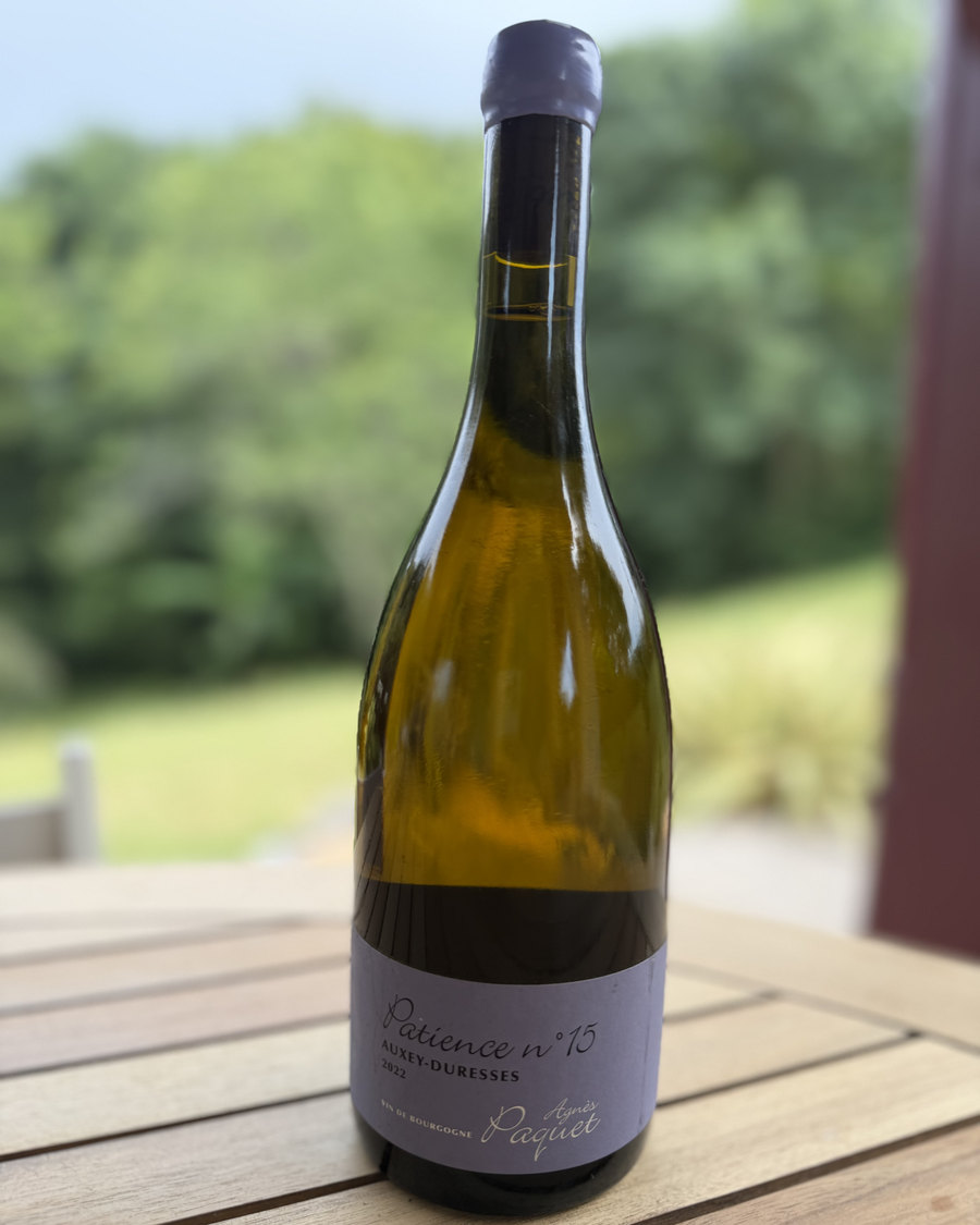 Bouteille d'Auxey-Duresses blanc « Patience n°15 » 2022 du Domaine Agnès Paquet, posée sur une table en bois face au vignoble.